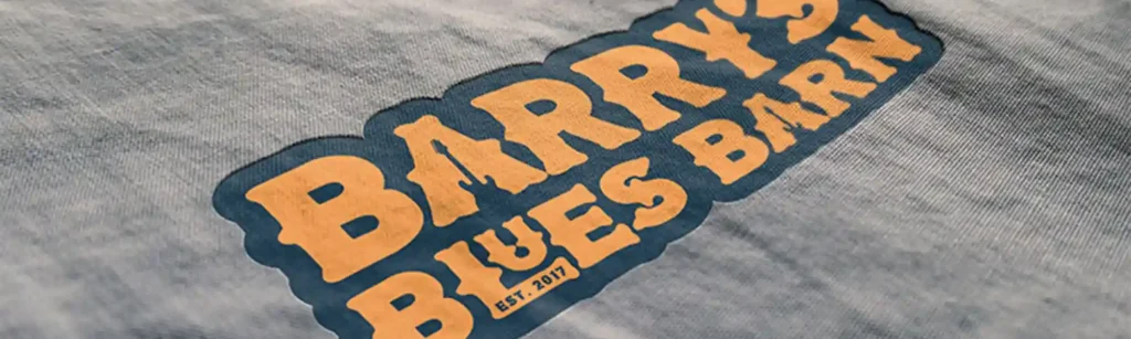 Close-up of a grey fabric with a logo printed on it, featuring bold orange and blue lettering, set within a bordered design, promoting a music-themed venue.
