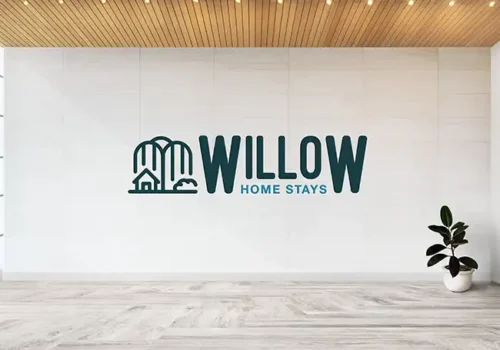 Minimalist logo for Willow Home Stays, featuring an outline of a house and willow trees alongside bold text, displayed on a modern, well-lit interior wall with wooden ceiling and potted plant.