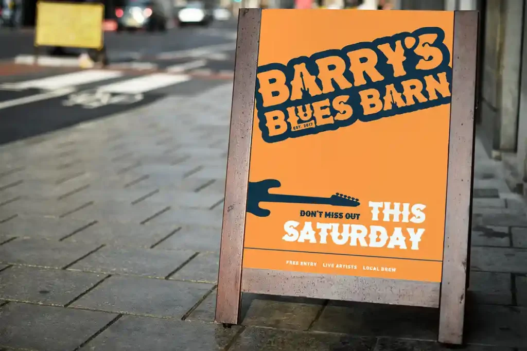 Street view of an orange sidewalk sign promoting a blues venue, featuring bold text and a guitar graphic, inviting passersby to a weekend gig.