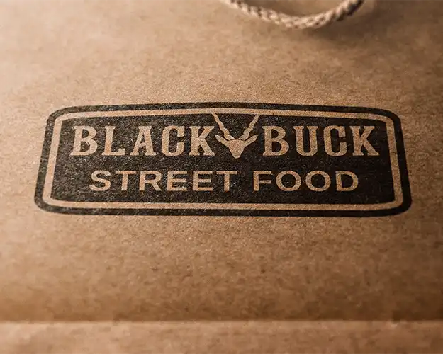 Close-up of a logo printed on a brown paper bag, featuring an oval design with a stylised deer head and antlers, and the text 'STREET FOOD' below the logo, all in a distressed black print.