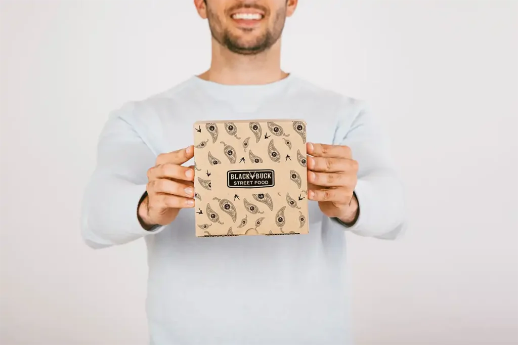 Person holding a cardboard food packaging with a detailed paisley pattern and the logo of a street food company printed on it.