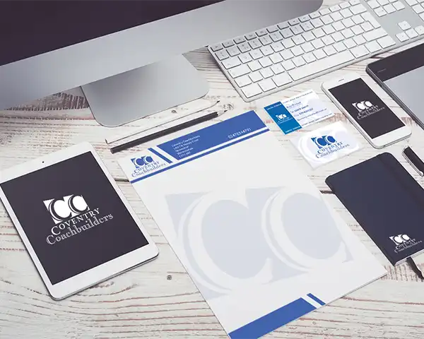 Professional coachbuilder branding materials displayed on a wooden desk, featuring stationery, business cards, and digital devices showcasing logo designs.