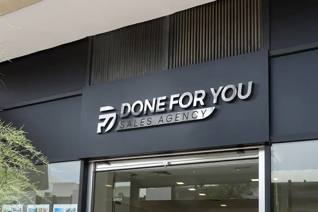 Modern office building facade with bold 3D lettering of a sales agency logo above the glass entrance door, featuring metallic and black design elements.