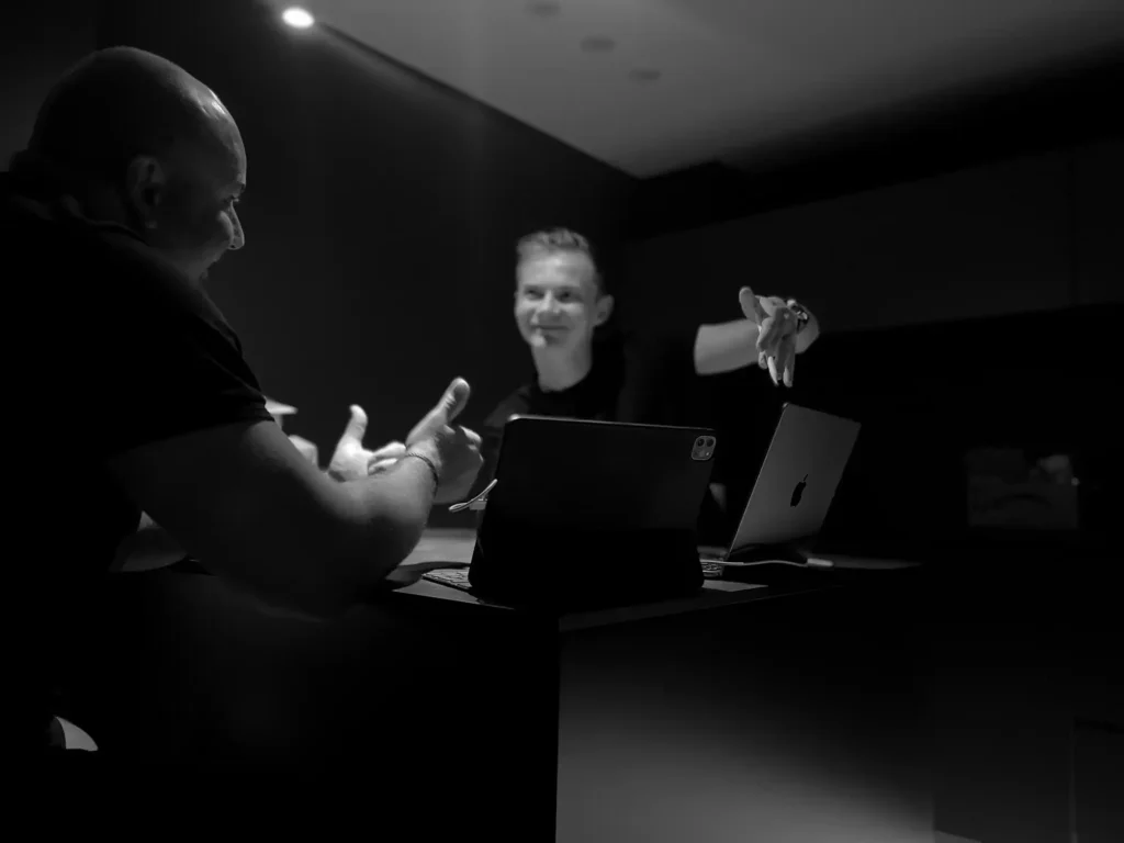 Monochrome image of a designer and client in a discussion at an office, one gesturing with his hand, with focused lighting on their faces.