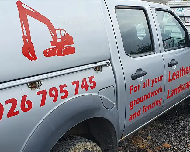 Side view of a work vehicle with red graphics including a digger icon and text advertising services for groundwork, fencing, and landscaping.