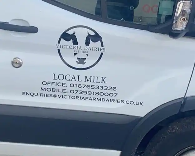 Side view of a delivery van branded with a dairy company logo and contact information, promoting local milk delivery.