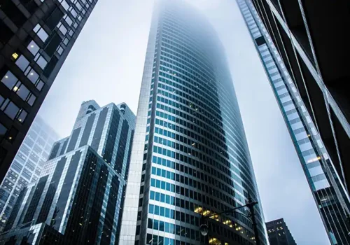 Low-angle view of modern skyscrapers in a city, with the tallest building disappearing into the foggy sky, emphasising urban architecture and atmosphere.