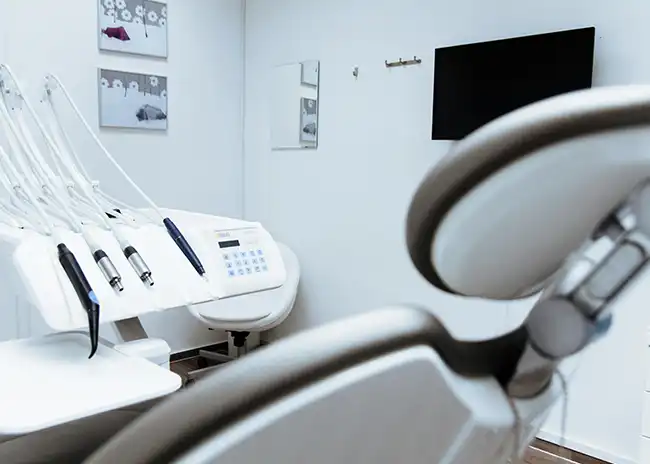 Modern dental clinic room featuring a dental chair, equipment, and a wall-mounted screen, with a clean and minimalist design.