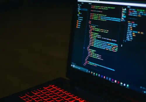 Close-up of a laptop screen displaying lines of code in a dark-themed text editor, with a red backlit keyboard, representing programming or software development.