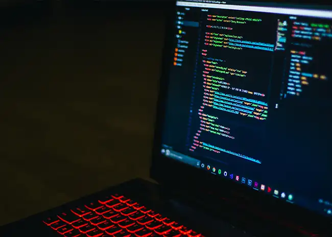 Close-up of a laptop screen displaying lines of code in a dark-themed text editor, with a red backlit keyboard, representing programming or software development.