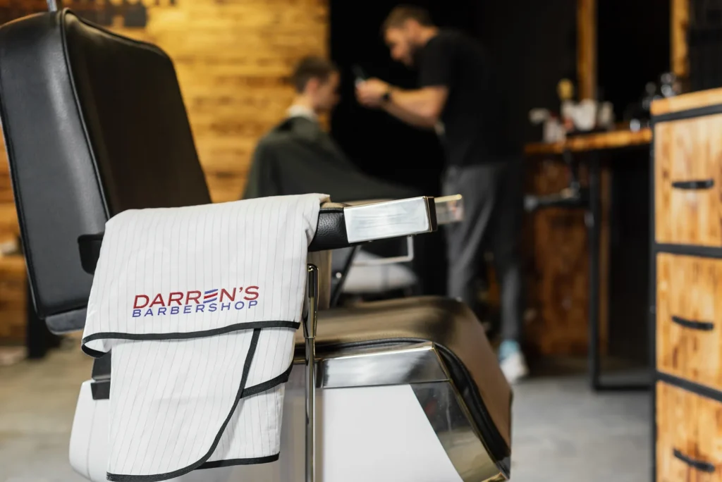 Barbershop logo design applied to towel on chair inside Darren’s Barbershop during haircut