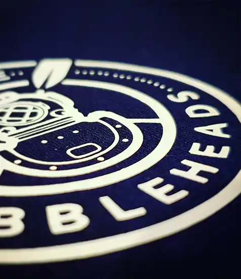 Close-up of custom printed Bobbleheads logo featuring a vintage diving helmet on navy fabric.