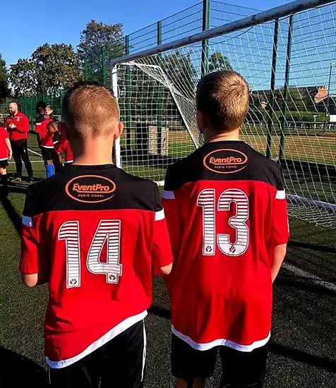 Custom printed football shirts with player numbers and sponsor logo for a youth team on a sunny outdoor pitch.