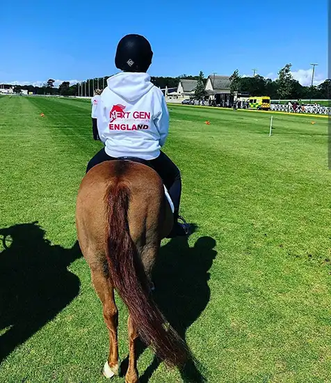 Rider wearing a custom printed "Next Gen England" hoodie on horseback at a sporting event in the UK.