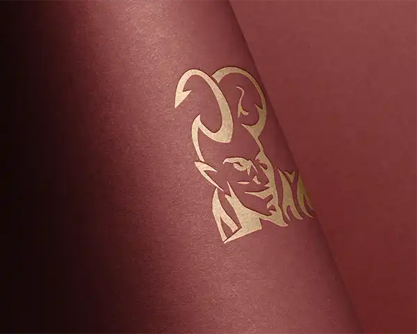 Gold foil devil logo design on textured burgundy paper – bold custom branding with metallic print finish