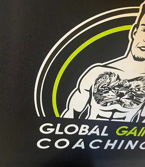 Custom printed “Global Gains Coaching” logo featuring a muscular figure with chest tattoo graphic on black fabric.